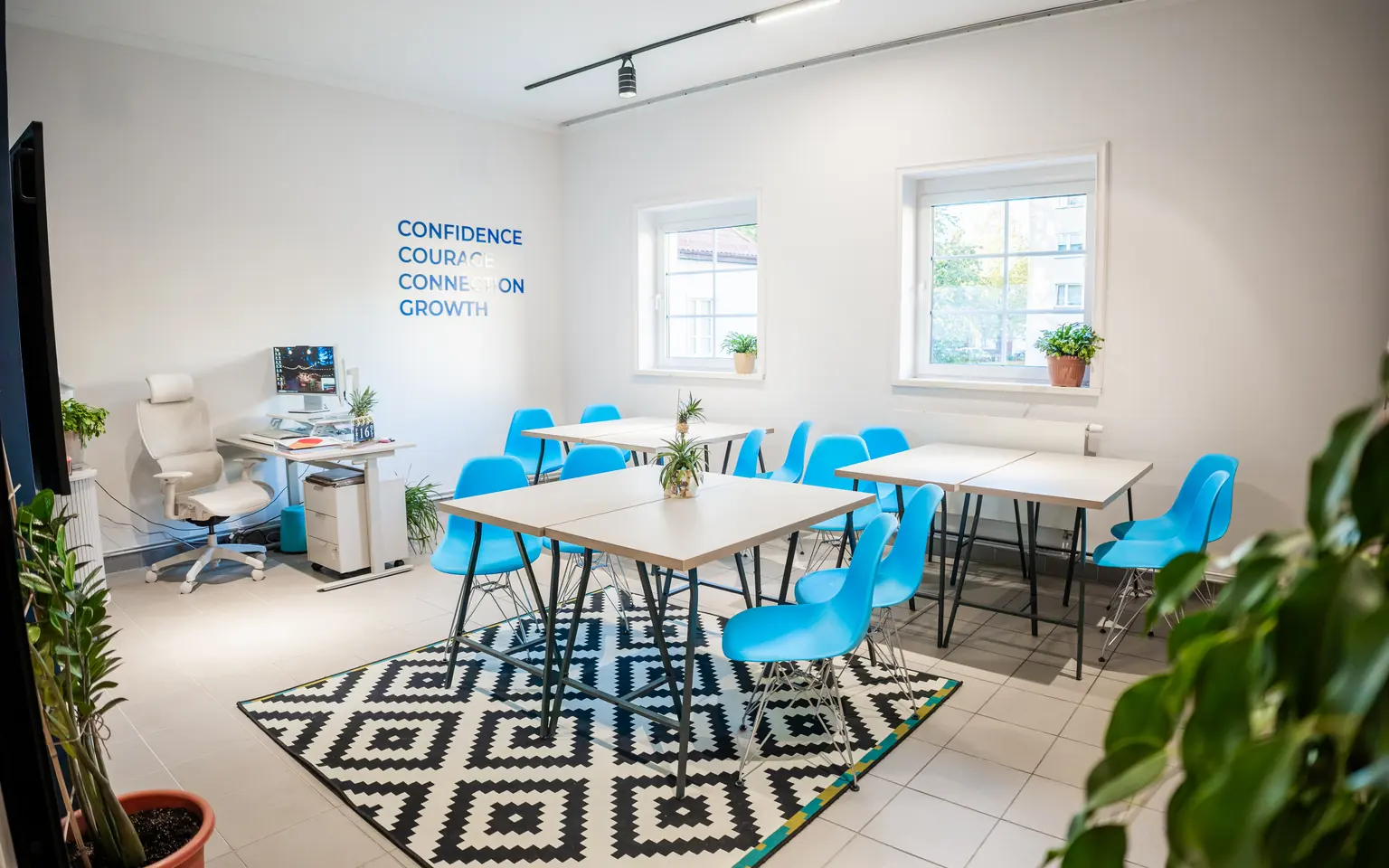 Wnętrze nowego Question House w Namysłowie - Learning Studio ze stołami, niebieskimi krzesłami i napisem Confidence, Courage, Connection, Growth na ścianie