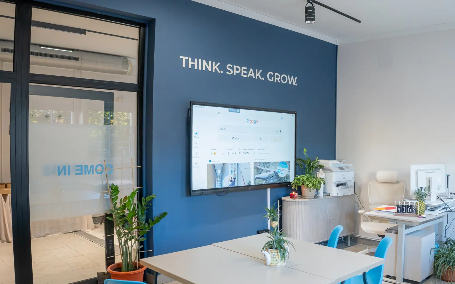 Granatowa ściana w Learning Studio Question House z napisem THINK. SPEAK. GROW. i 75-calowym monitorem