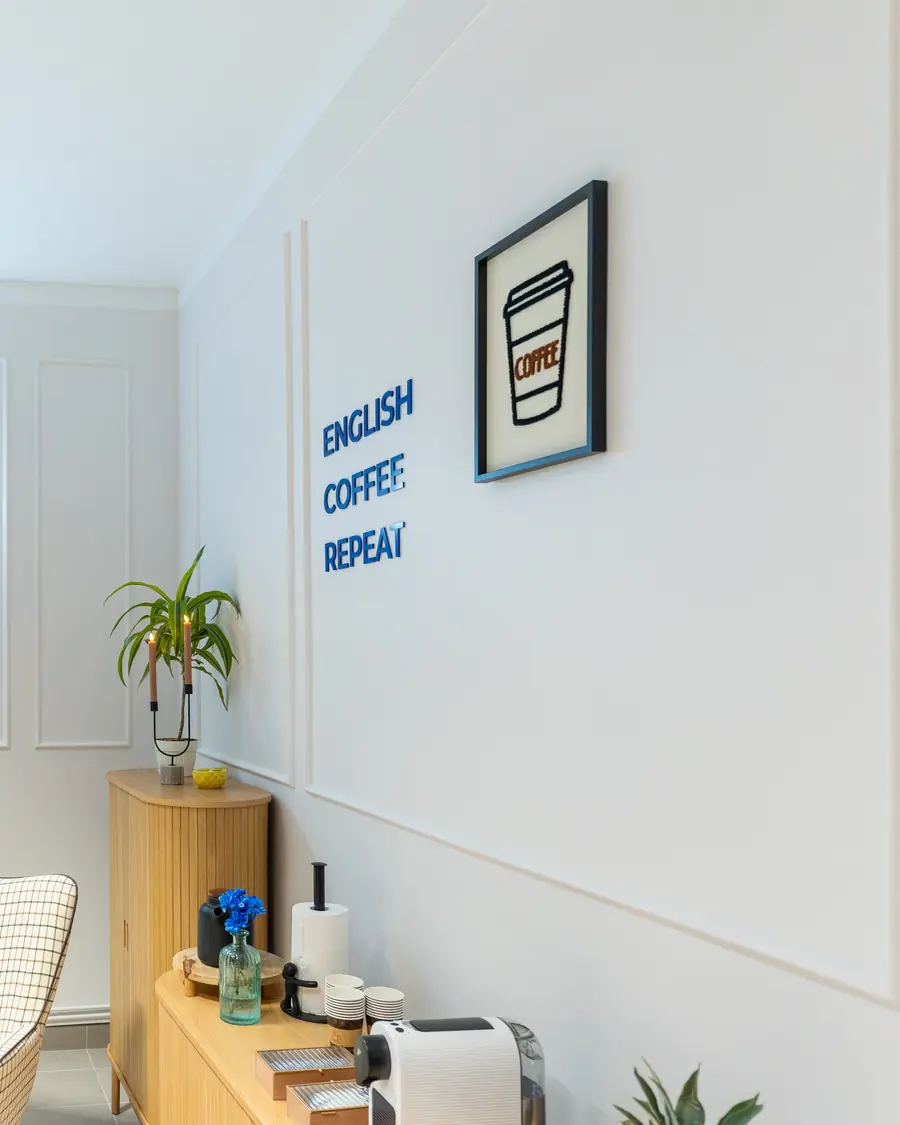 Coffee Spot w Question House - komoda z ekspresem do kawy i napis English, Coffee, Repeat na ścianie